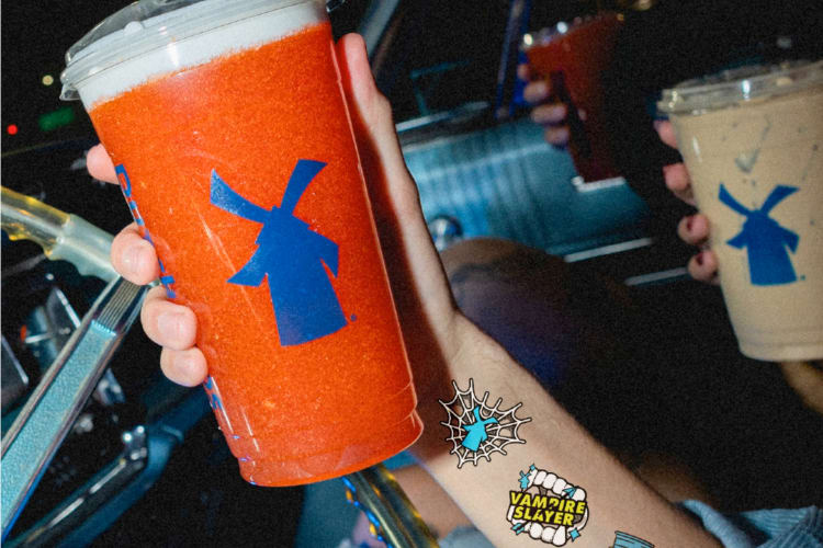 A person in a car holding a red-orange drink 