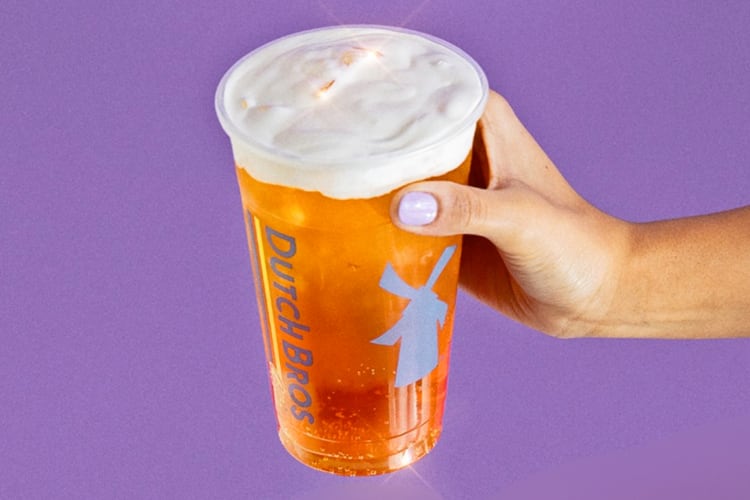 An orange drink with white foam on a purple background