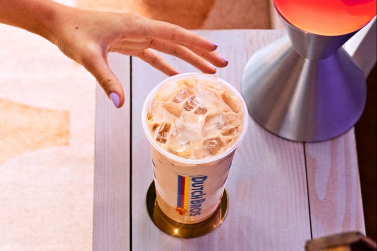 Someone reaching for an iced chai latte in a cup that says Dutch Bros