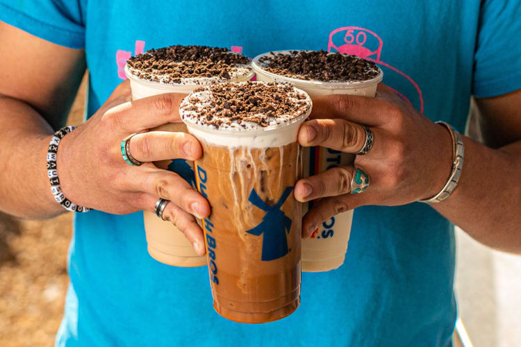 A person in a blue t-shirt holding three iced coffees