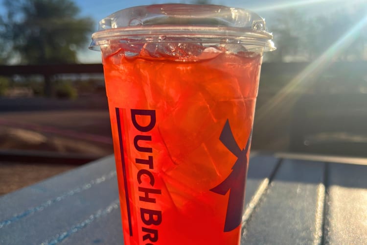 A red drink from Dutch Bros on a table outside