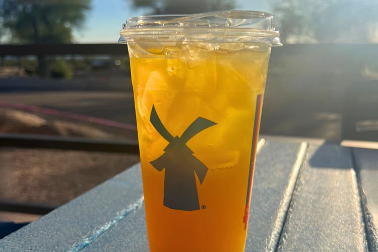 An orange drink from Dutch Bros on a table outside