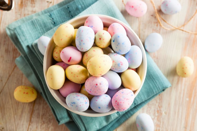 A person holding a white bowl of pastel coated chocolate mini eggs