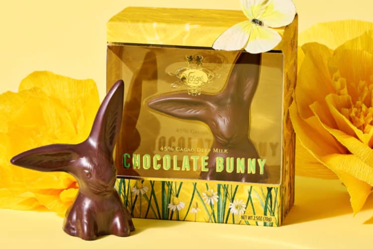 A chocolate bunny next to a yellow box with a butterfly atop it