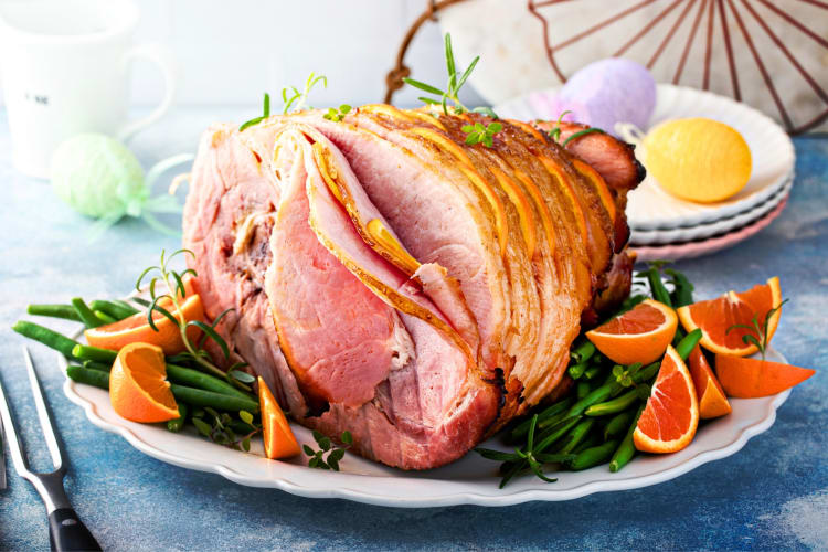 An Easter ham on a plate with green beans and orange slices