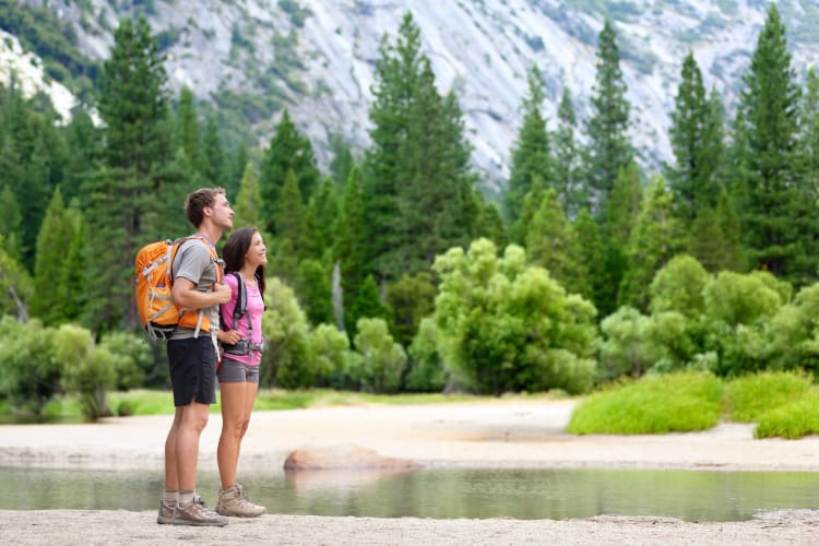 A couple in a park next to a lake, trees and mountains