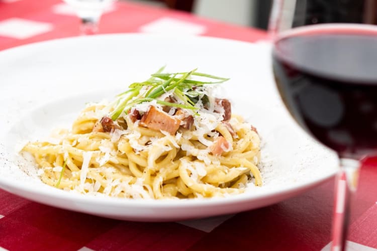 A plate of carbonara pasta and a glass of wine