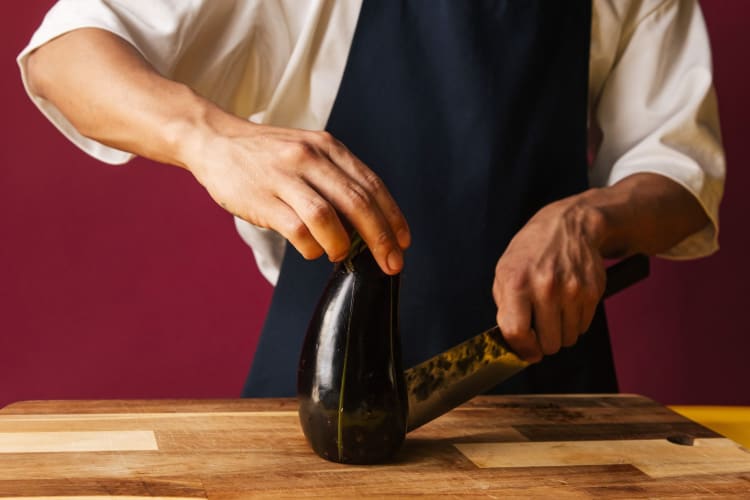 Can you freeze eggplant? Hands cutting up an eggplant on chopping board