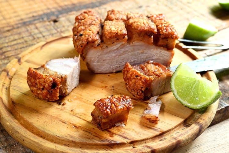 Chicharron with a lemon wedge on a wooden board