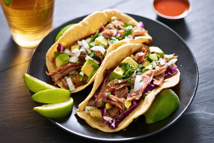 Two pork carnita tacos on a plate with lime wedges