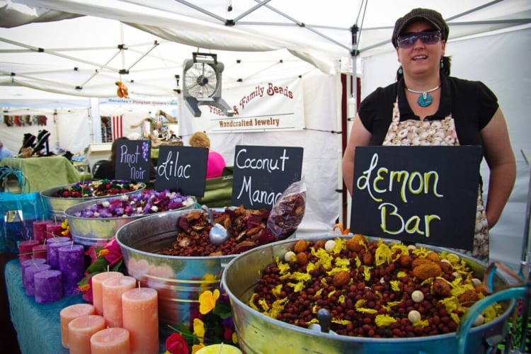 A woman at a festival stall selling different flavored foods and different types of candles