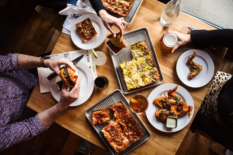 Aerial shot of three people eating a variety of foods at Emmy Squared
