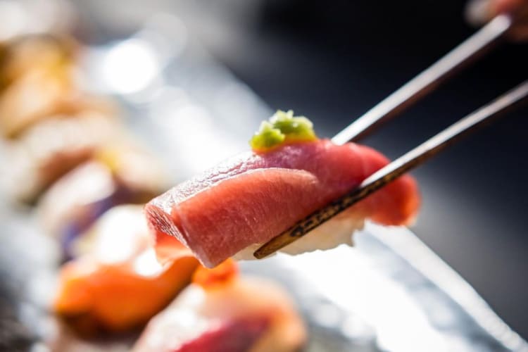 A person holding a piece of nigiri with chopsticks