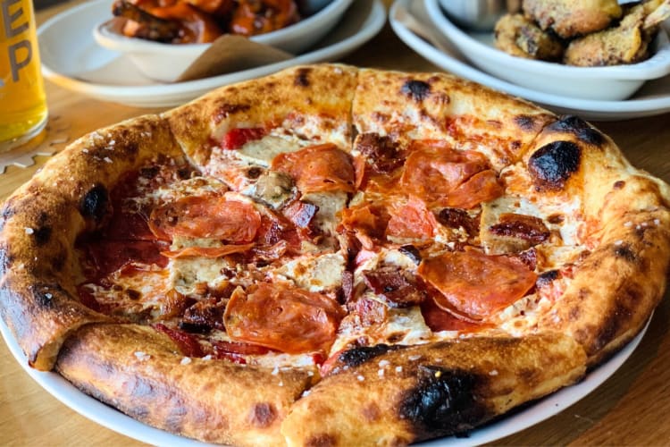 A meat pizza next to two bowls of wings