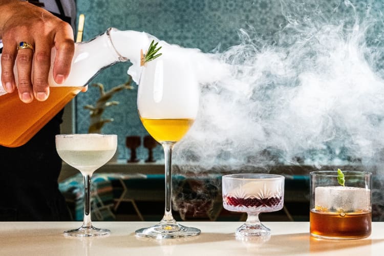 Four cocktails with steam being poured over them