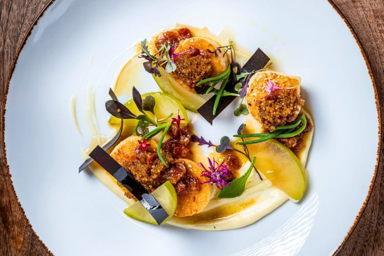 A plate with scallops, caviar and green garnishes