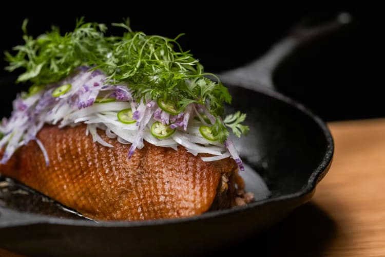 A duck dish with garnish in a cast iron pan