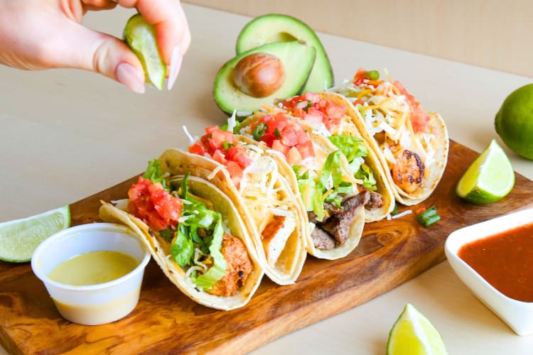 Tacos on a plate next to limes and avocados