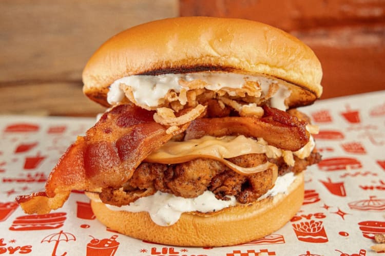 A sandwich with fried chicken, bacon, onions and sauce