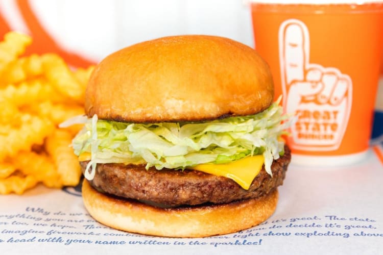 A burger with fries and a drink in an orange cup