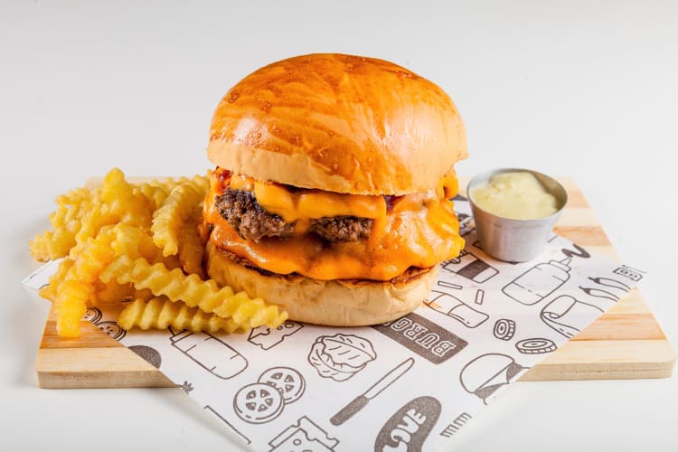 Fast food cheeseburger, fries and sauce on a wooden serving board