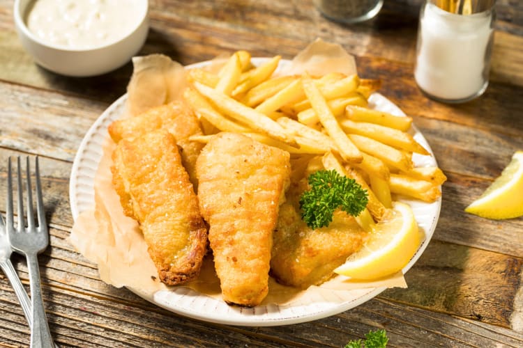 Fish and chips on a plate with a lemon wedge and garnish on top