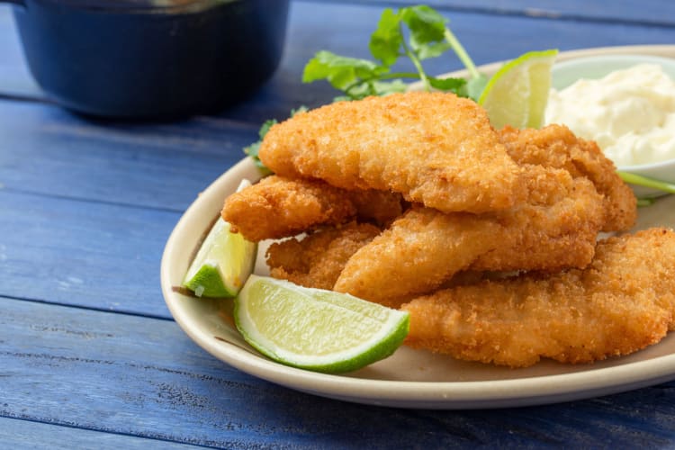 Fish strips on a white bowl with lemon wedges, sauce and garnish