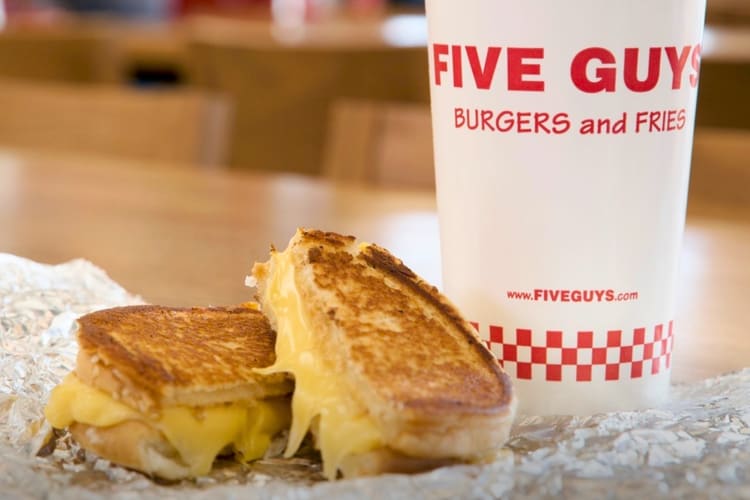 A grilled cheese next to a Five Guys cup