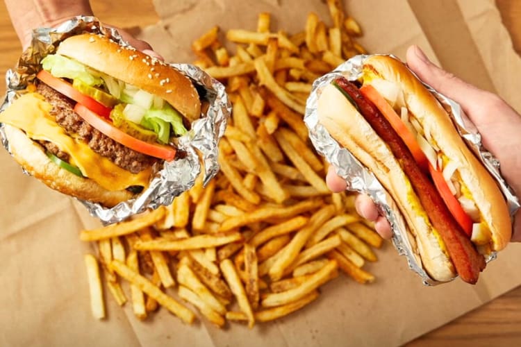 People holding a hot dog and a hamburger over fries on the table