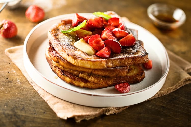 Slices of French toast topped with strawberries and powdered sugar