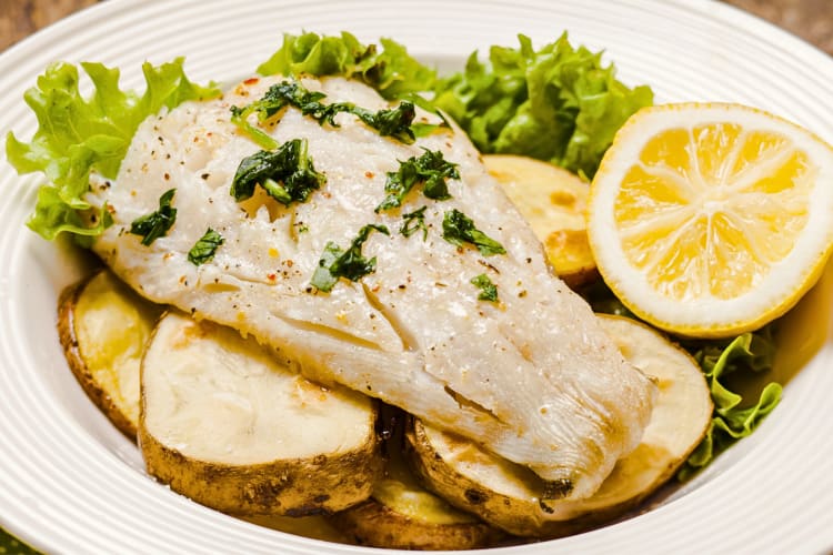 Cod served over potatoes and greens, with yuzu next to it and garnish on top