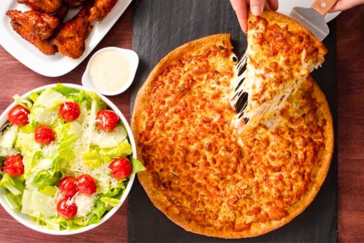 A pizza next to a salad and wings