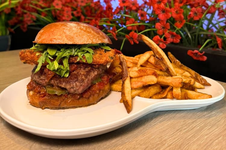 A burger and fries on a plate next to a bush with red flowers