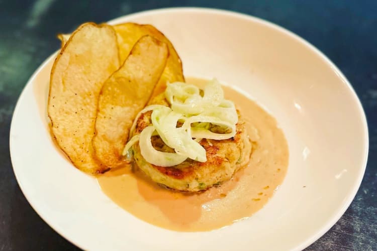 A blue crab cake served with white wine tarragon nage, crisp potato and fennel salad.
