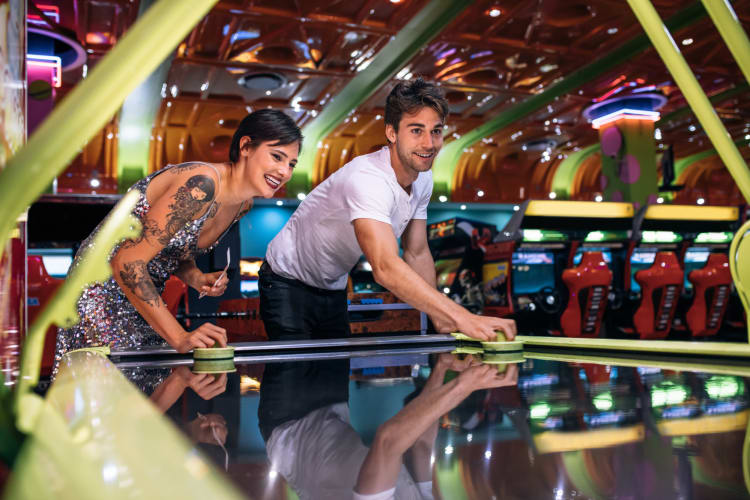 Two adult friends playing air hockey at an arcade arena