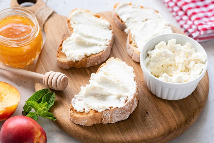 Ricotta cheese smeared on pieces of bread, served on a wooden board