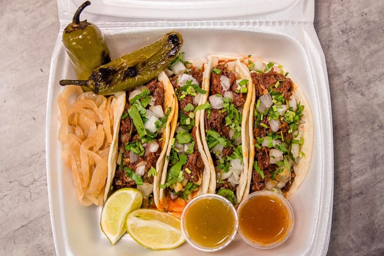 Aerial view of four tacos, two sauces, lemon wedges, onions and two jalapeños, from Fuel City