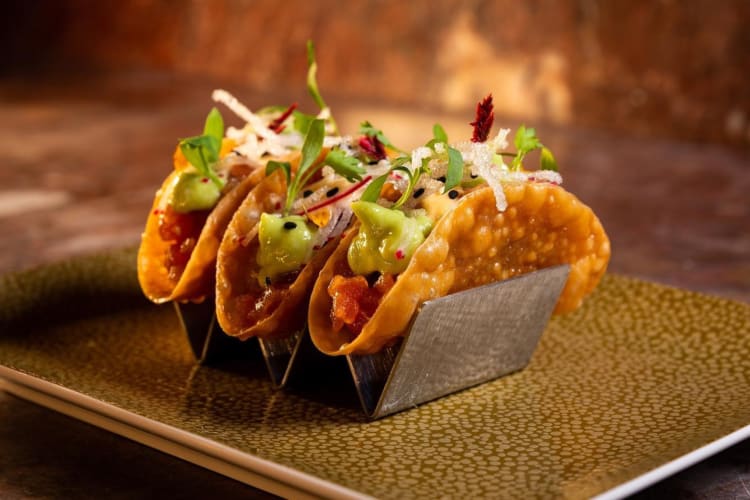 Three tacos in a stand on a gold patterned plate