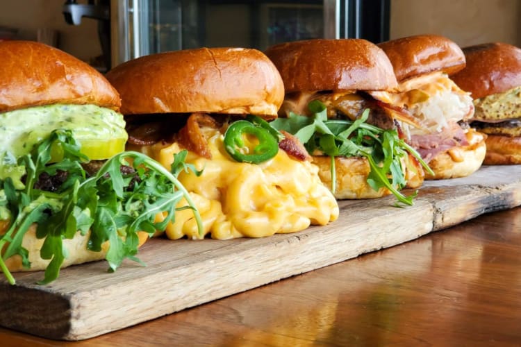 A row of loaded burgers on a wooden board