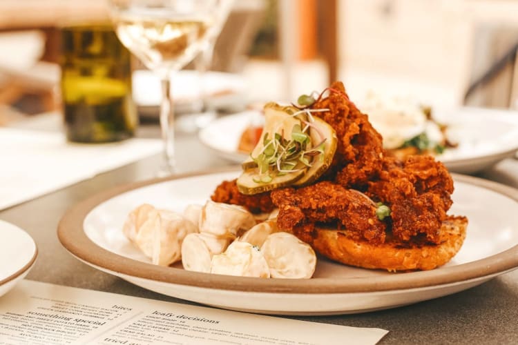 A dish with fried chicken on a table next to a wine glass and a menu