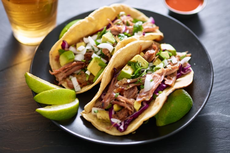 A plate of tacos with lime next to a pint of beer