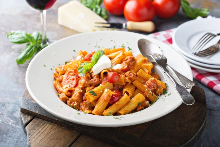 A bowl of rigatoni bolognese on a wooden table