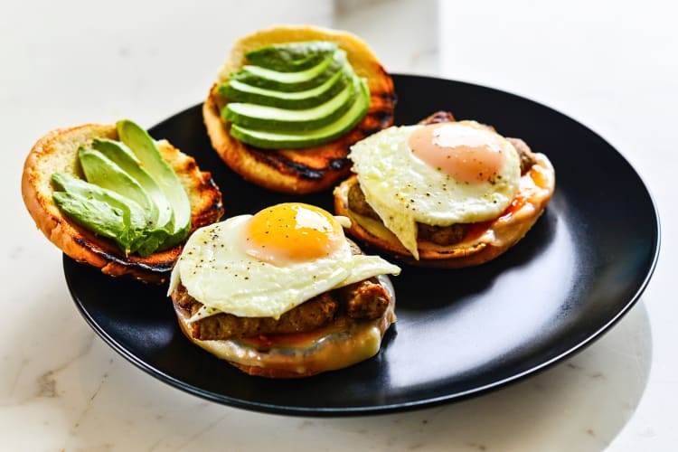 Two breakfast sandwiches with egg, sausage and avocado slices
