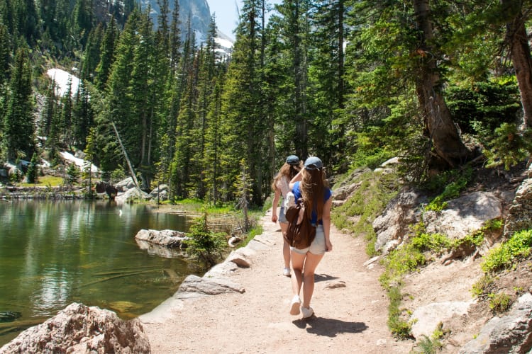 People on a hike next to a lake, trees and mountains