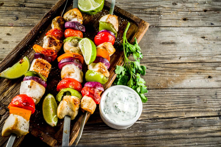 Vegetable and meat skewers and dip on a wooden surface