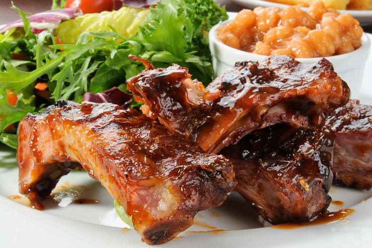 Baby back ribs with a green salad and baked beans in the background