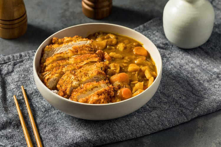 Katsu curry in a bowl next to a pair of chopsticks, all on top of a cloth
