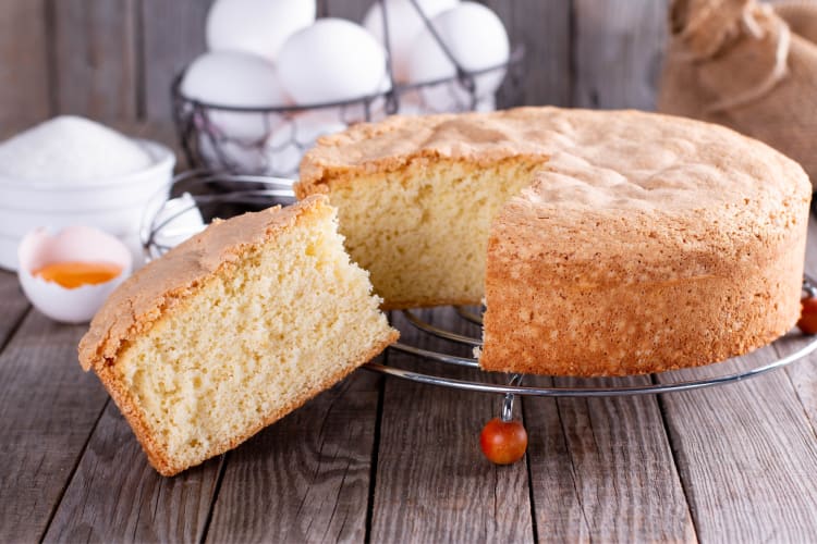 A sponge cake with a slice cut out next to eggs