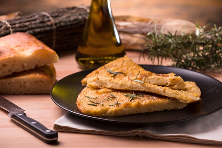 A thin chickpea bread-like dish next to olive oil and bread