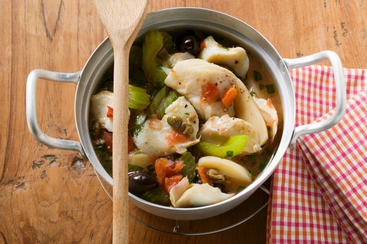 A pot with fish stew and a wooden spoon on top